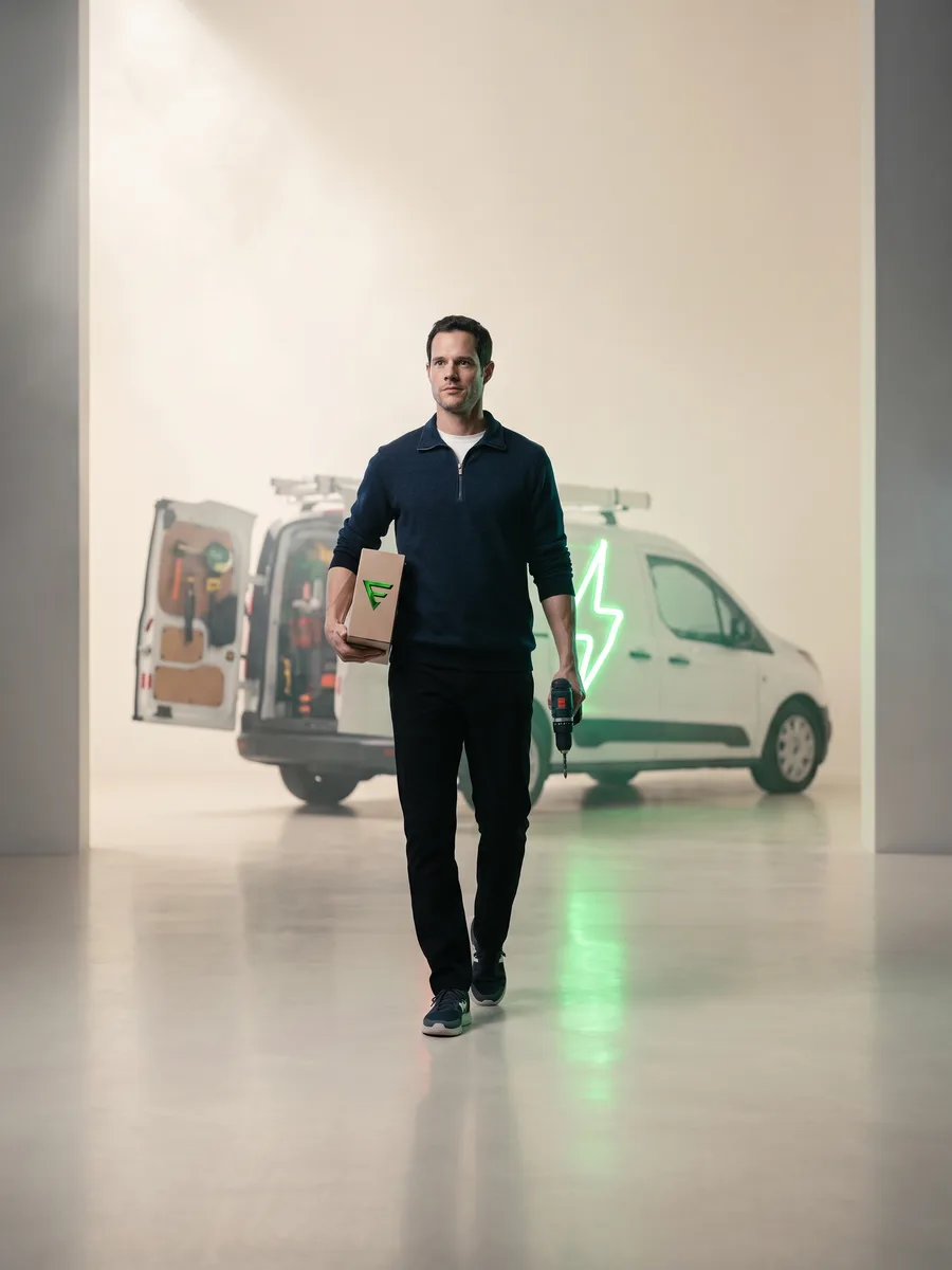 An electrician carrying a boxed charger past his work van, the bolt on its flank lit green